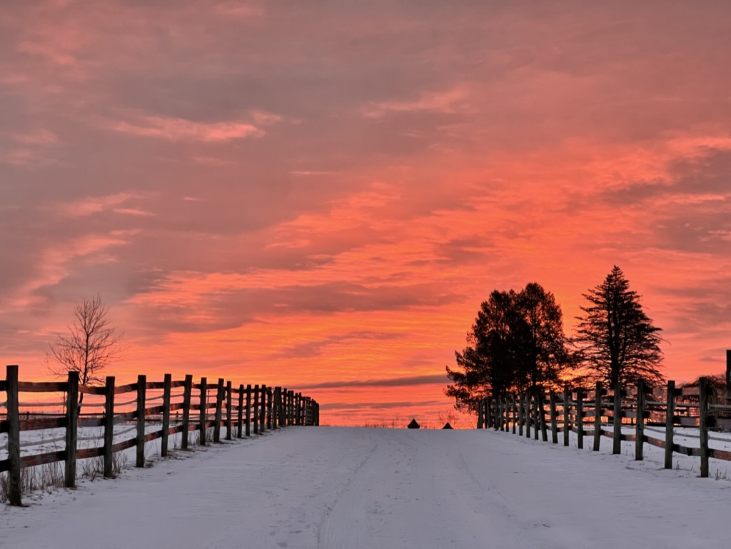 Winter sunset over the snowy farm road and post-and-rail fences